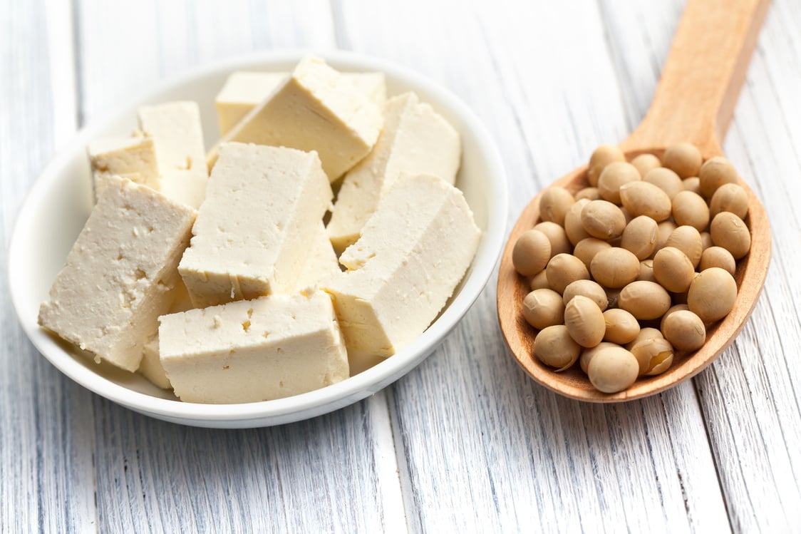 Bowl of tofu and spoonful of soybeans on wood surface